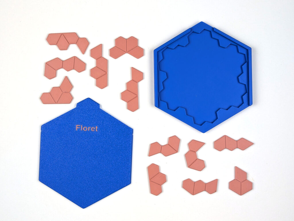 Zwölf Floret-Spielsteine neben der sechseckigen Box und dem Schiebedeckel mit der Aufschrift Floret